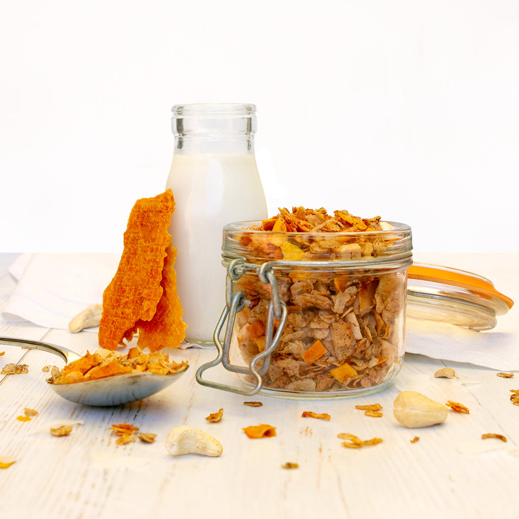 Dried Mango, Cashew and Coconut Granola in a clip top jar sitting in front of a bottle of milk